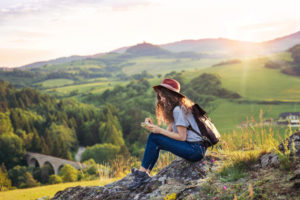 woman sitting on a mountaintop next to a forested valley