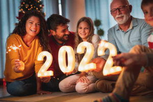 mom, dad, daughter, grandfather, and son sit together and hold a lighted "2022"
