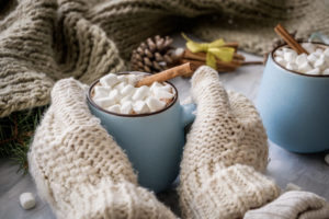 hands with mittens hold a cup of hot cocoa with marshmallows